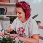 sitting sewing at a sewing machine with studio 7t7 club logo at the back