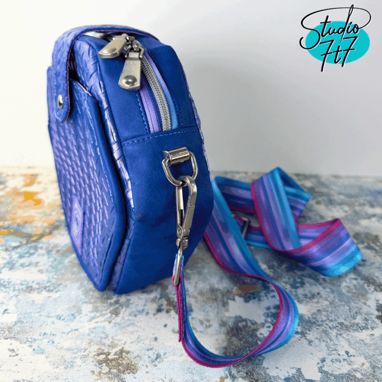 Side view of blue quilted hexagon cross body bag with zipper and striped woven strap – The Hexelle sewing pattern by Studio7t7